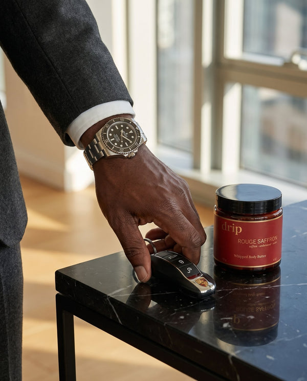 A man's hand in a charcoal suit and Rolex reaching for a Porsche key beside a jar of drip Rouge Saffron